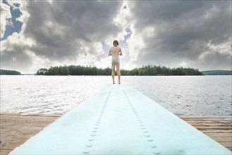 Caucasian girl standing on diving board over lake