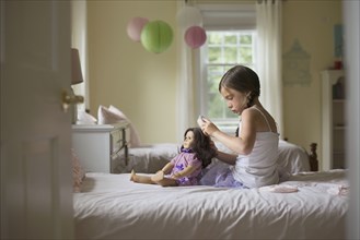Caucasian girl brushing hair of doll on bed