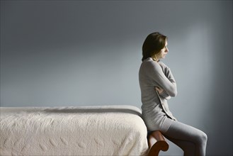 Sad Caucasian woman sitting on bed frame