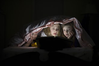 Caucasian sisters using laptop in blanket fort night