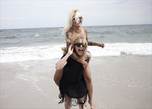 Woman carrying friend piggyback on beach