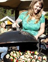 Smiling woman grilling kebabs in backyard