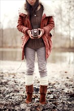 Caucasian woman photographing with vintage camera near rural pond