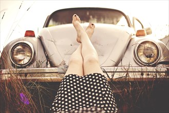 Caucasian teenage girl resting feet on vintage car