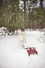 Caucasian girl pulling sled in snowy field
