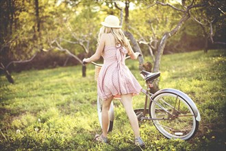 Woman pushing bicycle in rural field