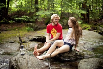 Couple sitting barefoot on boulders in forest