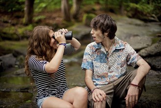 Couple using binoculars on boulders in forest