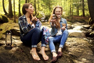 Girls blowing bubbles on forest rock