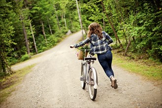 Rear view of girl pushing bicycle on dirt path