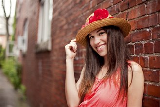 Smiling girl wearing straw hat near brick wall