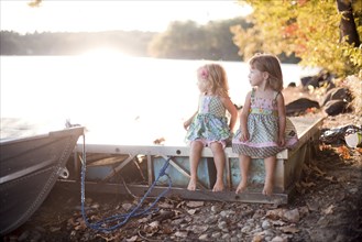 Girls sitting on wooden dock on rural lake