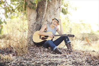 Caucasian musician holding guitar under tree