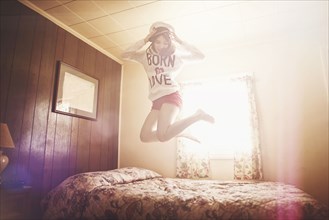 Caucasian girl in captain hat jumping on bed