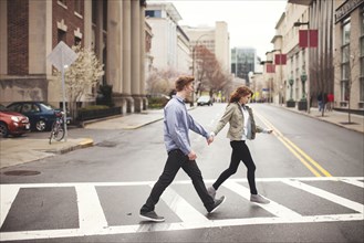 Caucasian couple holding hands crossing city intersection