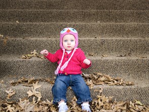 Baby girl sitting in autumn leaves on front steps