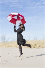 Woman in coat playing with umbrella on beach