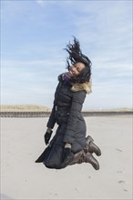 Woman in coat jumping for joy on beach