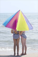 Caucasian girls under umbrella on beach
