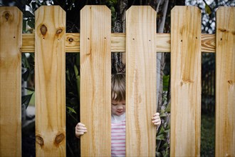 Mixed race girl looking through wooden fence in backyard