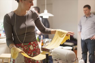 Woman rolling sheets of pasta in kitchen