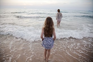 Mother and daughter walking in waves on beach