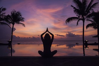 Silhouette of woman meditating near swimming pool at sunset