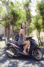 Woman sitting on scooter near trees