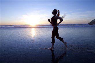 Silhouette of woman running on beach at sunrise