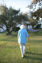 Caucasian woman walking with cane in backyard
