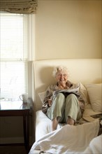 Older Caucasian woman reading newspaper in bed