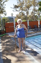 Older Caucasian woman standing with cane near swimming pool