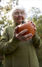 Older Caucasian woman admiring pumpkin outdoors