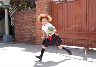 Smiling girl in school uniform running in driveway