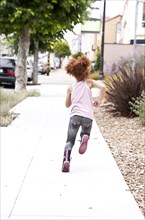 Rear view of girl running on city sidewalk