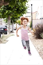Smiling girl running on city sidewalk