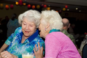 Older Caucasian women whispering at party in retirement home
