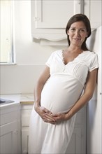 Pregnant woman holding her belly in kitchen