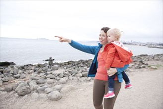 Caucasian mother holding daughter and pointing on beach