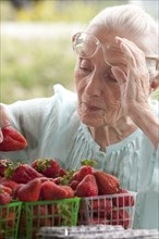 Older Caucasian woman examining strawberries at farmers market