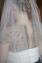 Rear view of Caucasian bride in veil with tattoos on back