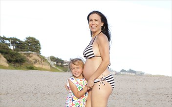 Pregnant Caucasian mother and daughter standing on beach