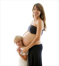 Smiling pregnant Caucasian mother hugging daughter