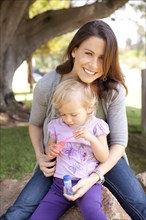 Caucasian mother and daughter blowing bubbles outdoors