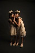 Whispering twin girls wearing crowns and princess costumes