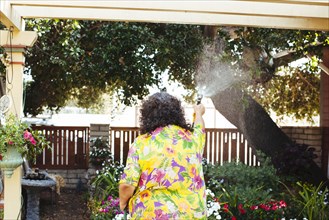 Hispanic woman watering plants in backyard