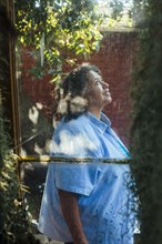 Hispanic woman behind window looking up in backyard