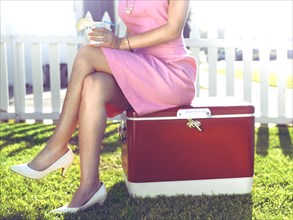 Glamorous woman sitting on vintage cooler in backyard