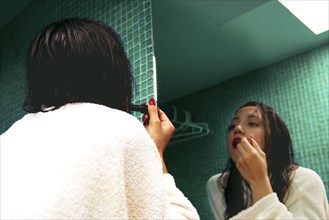 Mixed race woman applying makeup in mirror