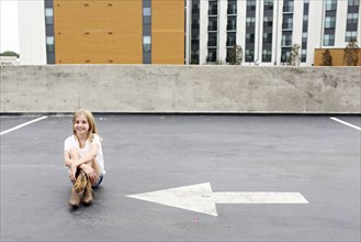 Teenage girl sitting on urban rooftop parking lot
